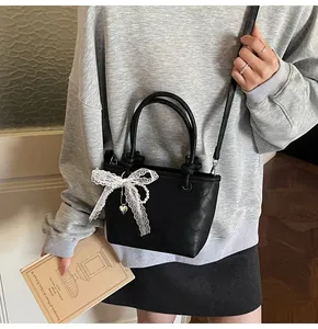Mini borsa tote nera opaca con fiocco in pizzo bianco e catena di perle su una modella