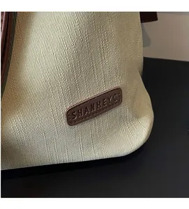 Detailed close-up of cream woven fabric texture and brown leather logo patch on tote bag