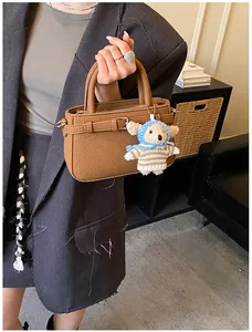 Close-up of brown litchi pattern leather handbag with a cute teddy bear charm