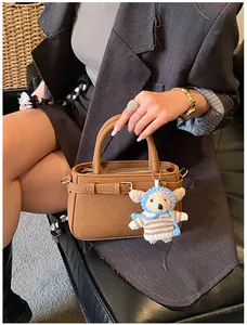 Detail of a brown lychee-pattern handbag featuring a cute knitted bear charm accessory