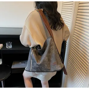 Detail of a large gray suede hobo bag with wide brown shoulder strap and zipper detail