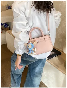 Detail of pink lychee leather handbag featuring a cute teddy bear plush charm and metal buckles