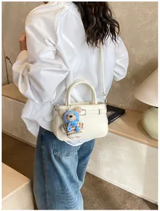 Detail of cream crossbody square bag featuring a cute teddy bear charm on leather texture