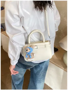 Close-up of cream textured leather handbag featuring a cute knitted bear charm on the side