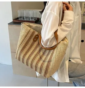 Detailed close-up of woven straw tote bag with brown leather straps and silver rivet details