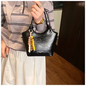 Detail der glänzenden schwarzen Beuteltasche mit bunter Perlenkette und Fashion-Schriftzug