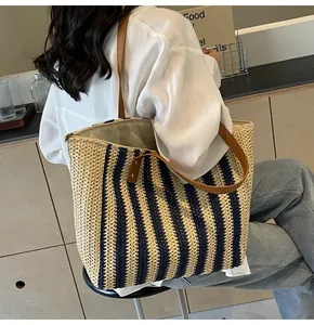 Detailed view of woven straw tote bag with navy stripes and brown leather shoulder straps