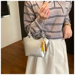 Detail der silbernen Metallic-Beuteltasche mit Riss-Textur und bunten Holzperlen-Anhänger