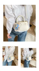 Close-up of white pebble leather handbag with decorative buckle and cute teddy bear charm