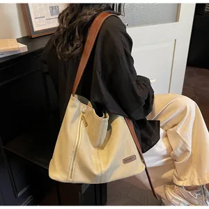 Close-up of a beige large tote bag featuring a decorative metal zipper and brown leather strap