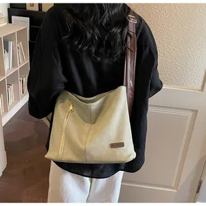 Close-up of beige canvas shoulder bag with brown leather straps and vertical zipper detail