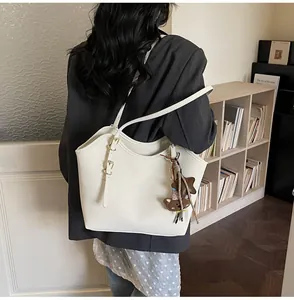 Detail of a large cream tote bag with gold hardware and bear charm on a female model