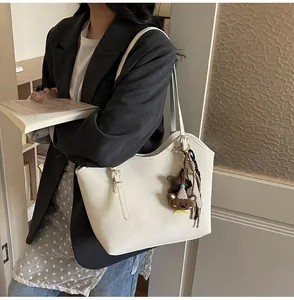 Detail of minimalist cream leather tote bag with a brown bear charm and metal hardware
