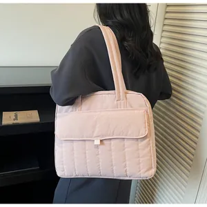 Close-up of a light pink quilted shoulder bag for laptops worn by a model in a minimal room