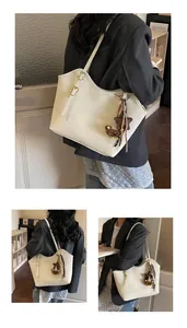 Detail view of large white leather tote bag with adjustable strap and cute bear charm