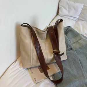 Large beige tote bag with dark brown straps and side zipper details on white bedding