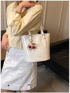 Detail of white glossy leather tote with cherry pendant and adjustable shoulder strap