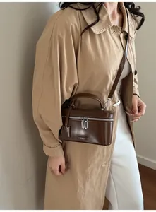 Détail d'un sac boîte en cuir mat marron foncé avec fermetures argentées et logo embossé