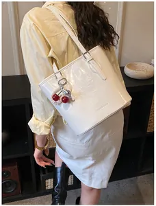 Detail of white patent leather shoulder bag with cherry and pearl charm on yellow shirt