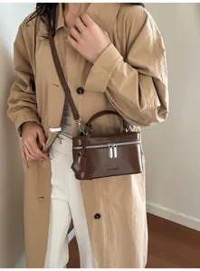 Détail d'un sac à bandoulière en cuir marron foncé porté avec un trench élégant