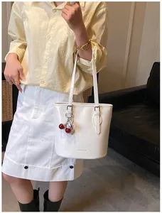 Close-up of a white glossy shoulder bag featuring a cherry charm and pearl detail