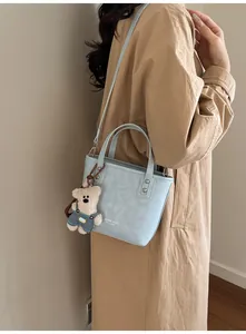 Détail du sac bandoulière bleu clair avec breloque ours et marquage sur le manteau
