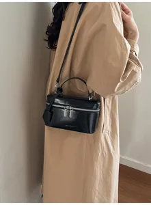 Détail d'un sac à main carré noir avec fermetures éclair argentées porté par un mannequin