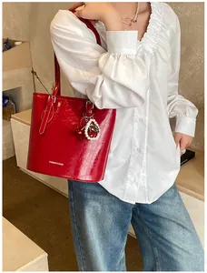 Detail of red glossy bucket bag with pleated texture and pearl cherry charm