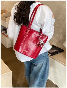 Side view of red patent leather tote bag with cherry charm on a model for daily commute