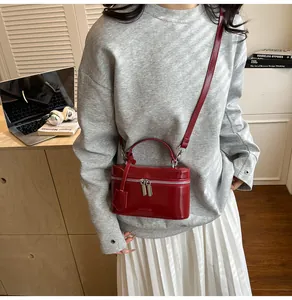Sac boîte rouge verni porté avec un pull gris et une jupe plissée blanche