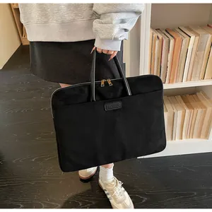 Detail van minimalistische zwarte laptoptas van suède met gouden ritsen en leren merklogo