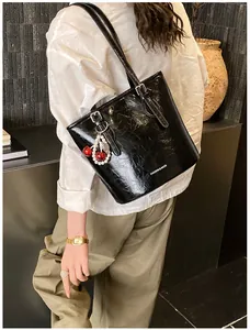 Detail of glossy patent leather shoulder bag with fashion text and cherry pearl charm