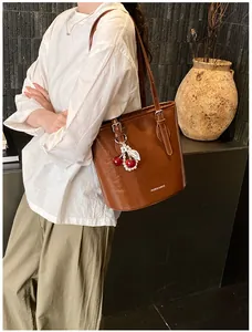Detailed side view of a brown vintage bucket bag with red cherry charm and thin strap