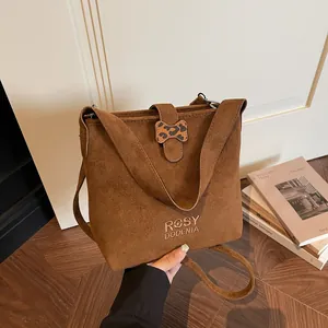 Brown suede bucket bag with embroidery and leopard print bow on a warm minimalist background