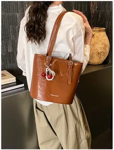 Detail of a brown glossy leather shoulder bag with cherry pendant and silver buckle