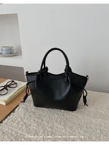 Detailed close-up of a black matte PU leather tote bag with knot handle on soft fabric