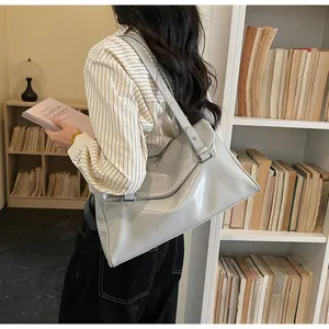 Detailed view of grey glossy patent leather tote bag on shoulder in a cozy library setting