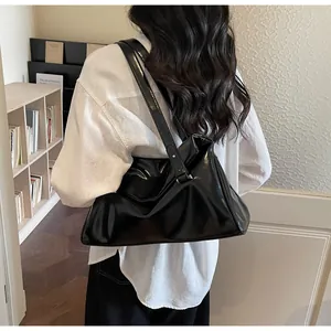 Detailed view of black glossy patent leather shoulder bag on model with white shirt