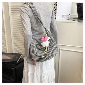 Detail of checkered hobo bag with a plush bunny charm worn by a model in a modern room
