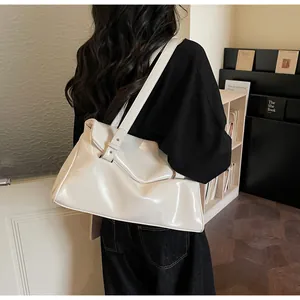 Shoulder shot of a cream white patent leather tote bag with glossy finish on a model