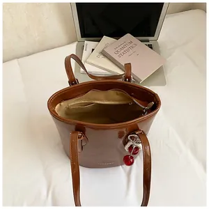 Brown gloss leather tote bag with cherry charm and large interior shown on white bedding