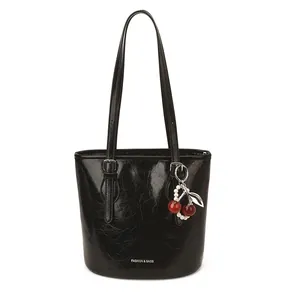 Glossy black bucket shoulder bag with cherry charm and fashion logo on white background