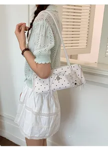 Close-up of white polka dot shoulder bag with bow, heart pendant and plush bear charm