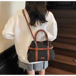 Dettaglio di borsa tote in tela nera con spalline in pelle marrone su modella