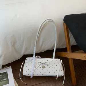 Close-up of stylish polka dot baguette bag featuring heart pendant and lace strap detail
