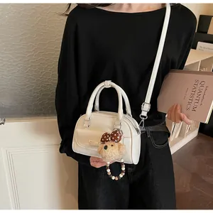 Détail d'un sac Boston blanc en similicuir avec un ours en peluche et un nœud décoratif