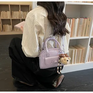 Détail d'un sac violet clair avec nœud et breloque ours dans un décor de bibliothèque