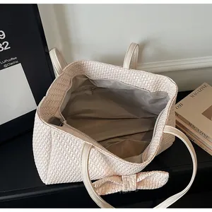 Close-up of off-white woven tote bag showing internal zipper pocket and bow detail