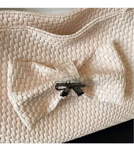 Close-up of beige woven tote bag featuring a large bow and black metal accent
