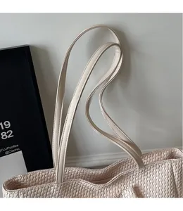 Detail of a cream woven tote bag featuring smooth, long shoulder straps and fine texture